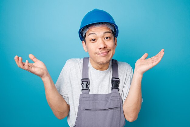 Clueless young construction worker portant un casque de sécurité et l'uniforme faisant je ne sais pas de geste