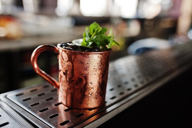 Cocktail alcoolisé à la menthe glacée et au citron vert dans une tasse en bronze sur une table de bar