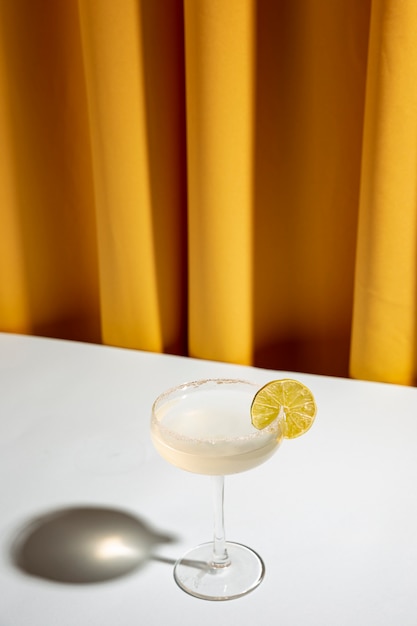 Cocktail de citron vert dans une soucoupe de champagne sur un bureau blanc contre un rideau jaune