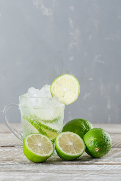 Cocktail mojito glacé aux limes dans une tasse en verre sur fond de bois et de plâtre, vue latérale.