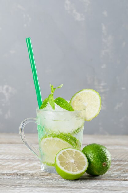 Cocktail mojito glacé dans une tasse de limes, paille, menthe vue latérale sur fond de bois et de plâtre