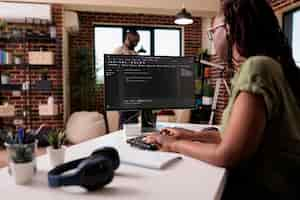 Photo gratuite une codante développant des logiciels pour un projet indépendant travaillant à distance de chez elle pendant que son petit ami se détend. un programmeur afro-américain écrivant du code source à la recherche d'erreurs lors du débogage.