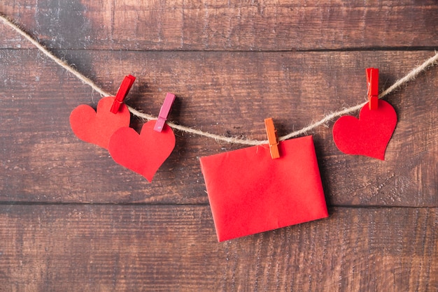 Photo gratuite coeurs et enveloppe en papier rouge avec des épingles accrochées au fil