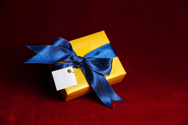 Coffret cadeau doré avec noeud bleu sur fond rouge