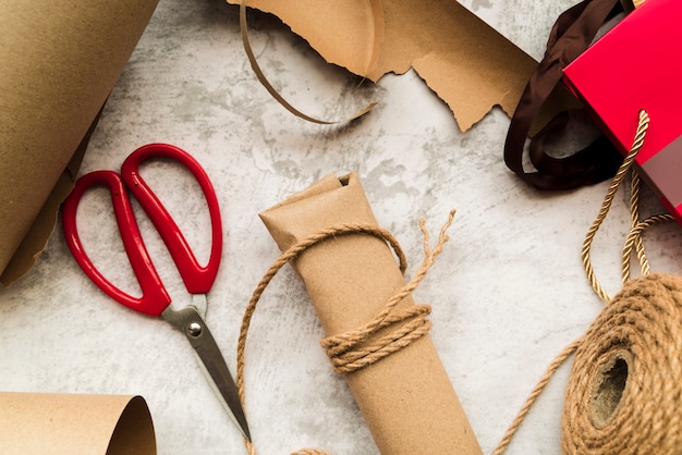 Coffret cadeau enveloppé marron avec ficelle et ciseaux sur fond texturé blanc