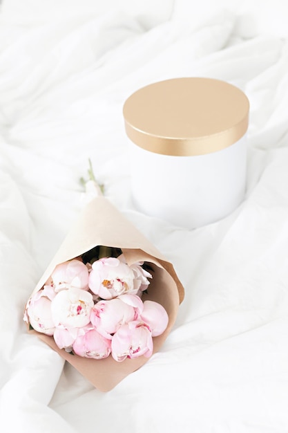 Coffret or sur le lit Bouquet de pivoines blanches dans un emballage artisanal Intérieur blanc scandinave