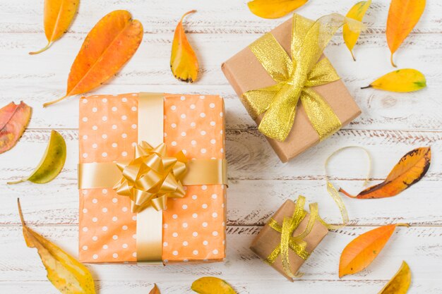 Coffrets cadeaux décoratifs entourés de feuilles orange sur une table blanche