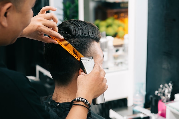 Coiffeur asiatique tenant un peigne et tondeuse à la tête du client