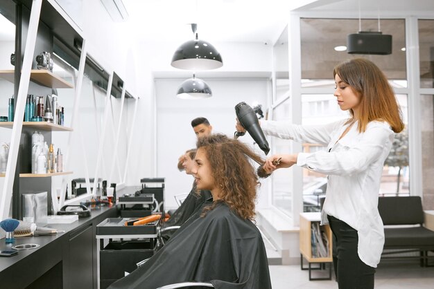 Coiffeur féminin séchant les cheveux bouclés de la fille à l'aide d'une grande brosse en plastique