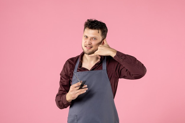 coiffeur homme vue de face avec brosse à cheveux et ciseaux sur fond rose