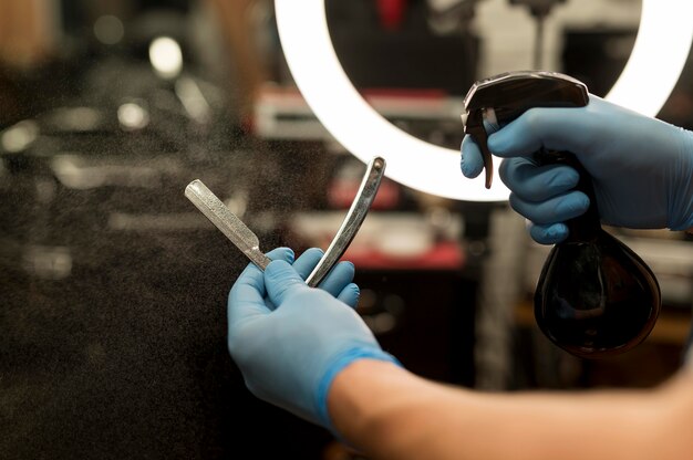 Coiffeur masculin avec des gants en latex tenant un jet d'eau et une lame de rasoir