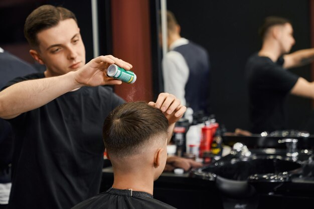 Coiffeur poudrant les cheveux d'un client masculin pour fixer la coupe de cheveux