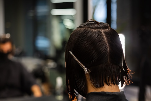 Un coiffeur professionnel fait une coupe de cheveux à un client. La jeune fille est assise dans un masque de beauté le salon