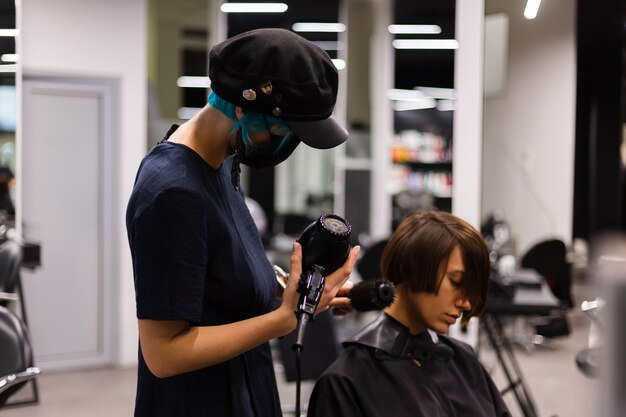 Un coiffeur professionnel fait une coupe de cheveux à un client. La jeune fille est assise dans un masque de beauté le salon