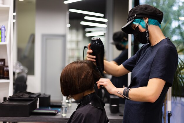 Un coiffeur professionnel fait une coupe de cheveux à un client. La jeune fille est assise dans un masque de beauté le salon