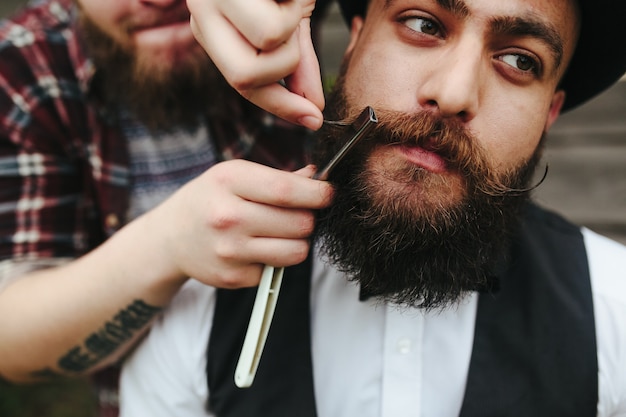 Photo gratuite le coiffeur rase un homme barbu dans une atmosphère vintage