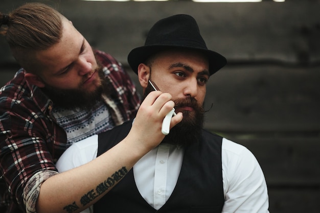 Le coiffeur rase un homme barbu dans une atmosphère vintage