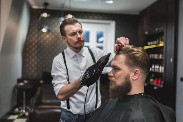 Coiffeur séchant les cheveux de beau client