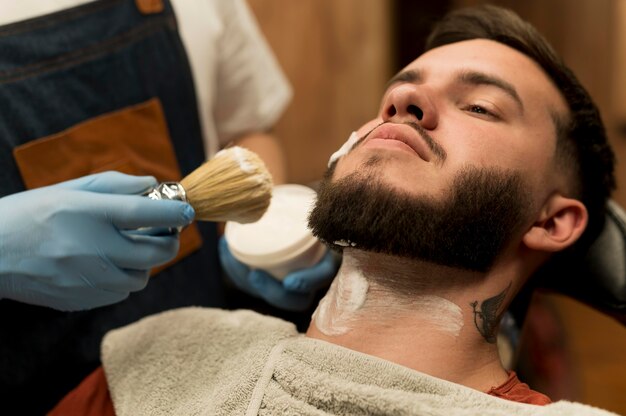 Coiffeur utilisant de la crème à raser pour contourner la barbe du client masculin