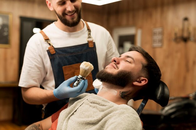 Coiffeur utilisant de la crème à raser pour contourner la barbe du client masculin