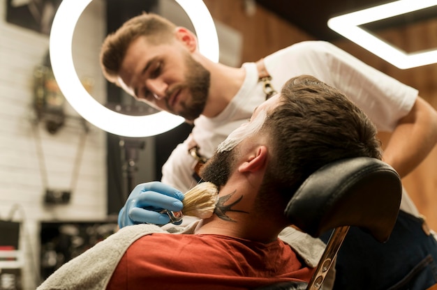 Coiffeur utilisant de la crème à raser pour contourner la barbe du client masculin