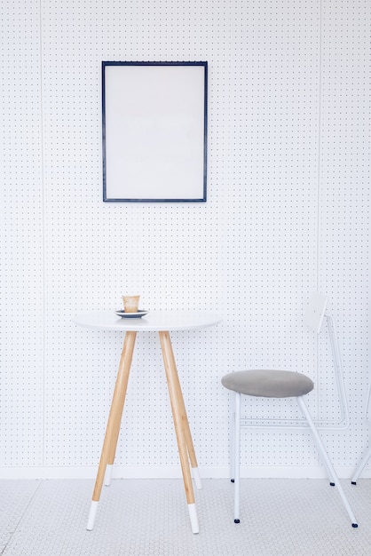 Coin d&#39;une cuisine avec table, chaises grises et une affiche suspendue sur un mur gris clair.
