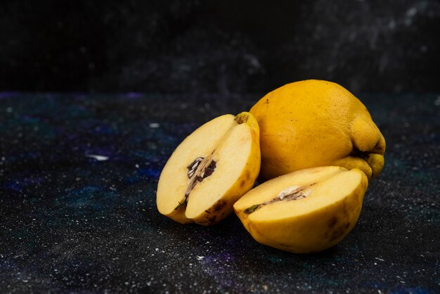 Coings mûrs entiers et tranchés placés sur une table sombre.