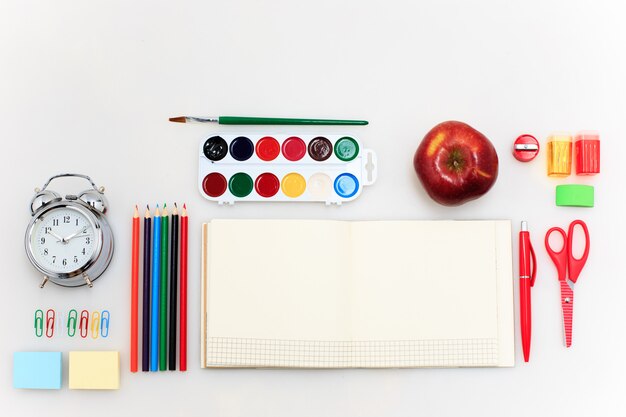 École avec cahiers, crayons, pinceau, ciseaux et pomme sur blanc