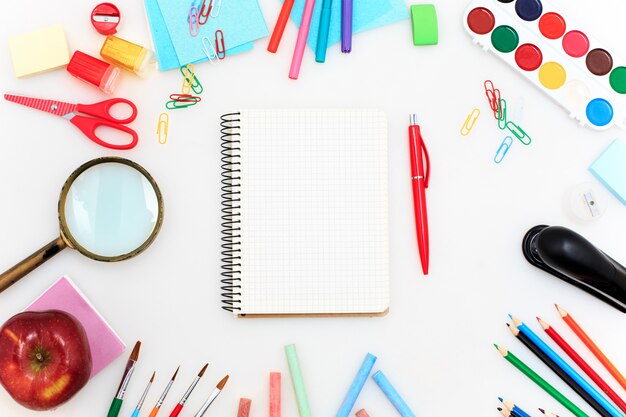 École avec cahiers, crayons, pinceau, ciseaux et pomme sur blanc