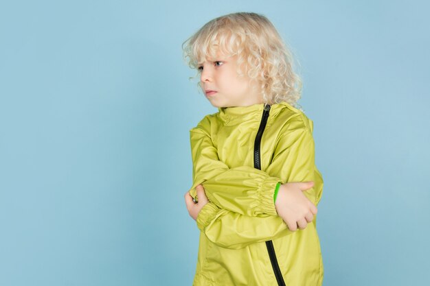 En colère, triste. Portrait de beau petit garçon caucasien isolé sur mur bleu. Modèle masculin blond bouclé. Concept d'expression faciale, émotions humaines, enfance