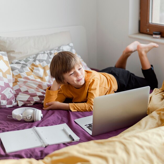 Écolier assis dans son lit avec son ordinateur portable