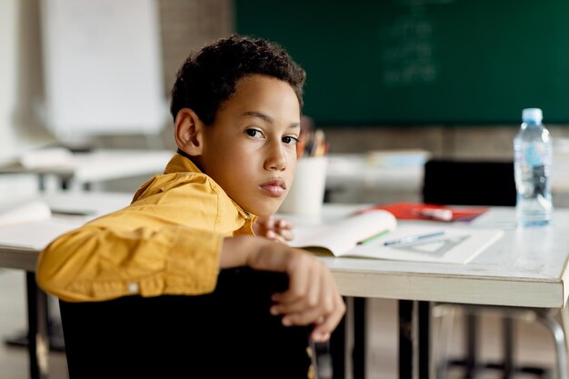 Écolier noir se tournant vers la caméra alors qu'il était assis dans la salle de classe