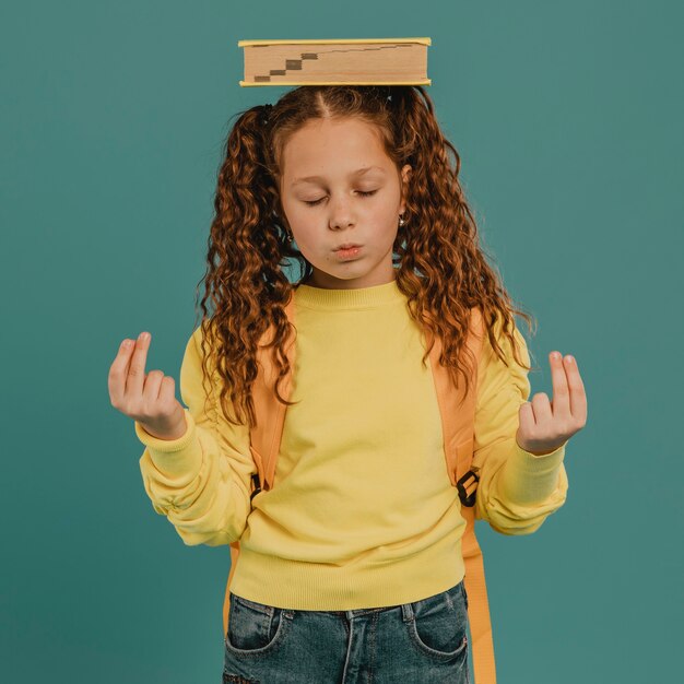 Écolière avec chemise jaune tenant un livre sur la tête