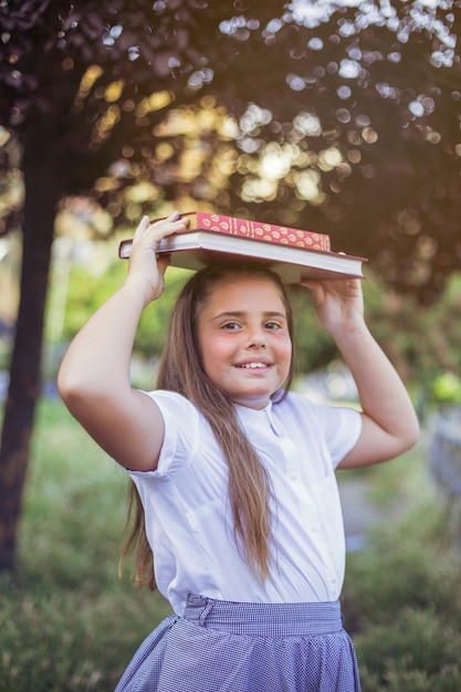 Écolière debout avec des livres sur la tête en souriant