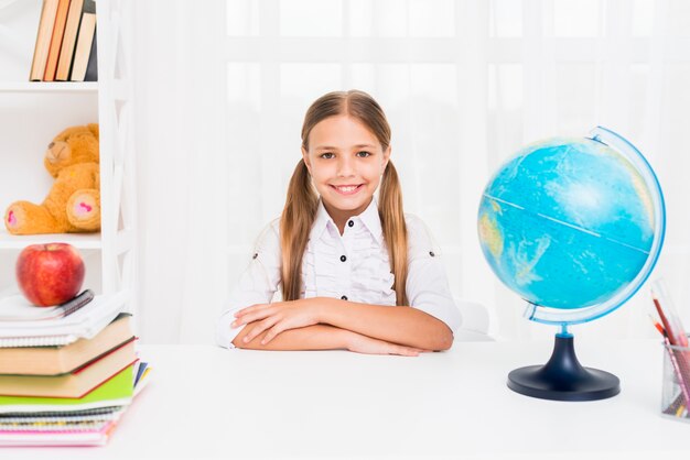 Écolière diligent assis à la table à côté du globe dans la salle de classe