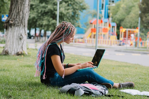 Écolière élégante dans le parc avec un ordinateur portable