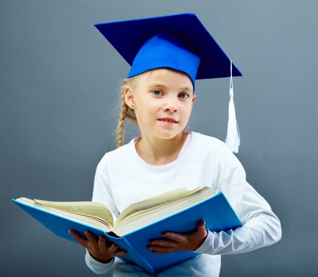 Écolière avec graduation cap tenant un livre lourd