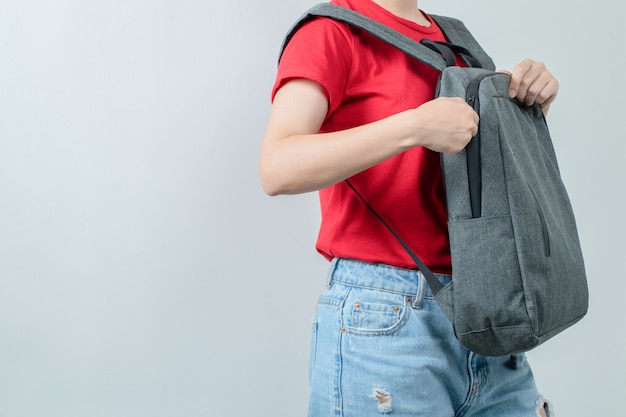 Écolière portant son sac à dos gris aux épaules.