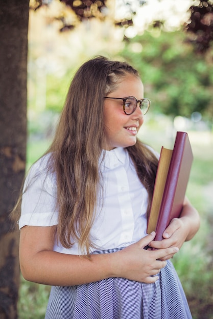 Écolière en uniforme debout dans le jardin avec des livres