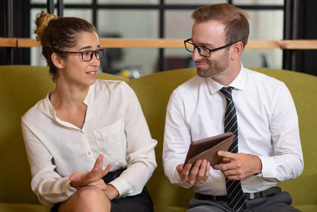 Collaborateurs utilisant une tablette et se disputant dans le hall du bureau.