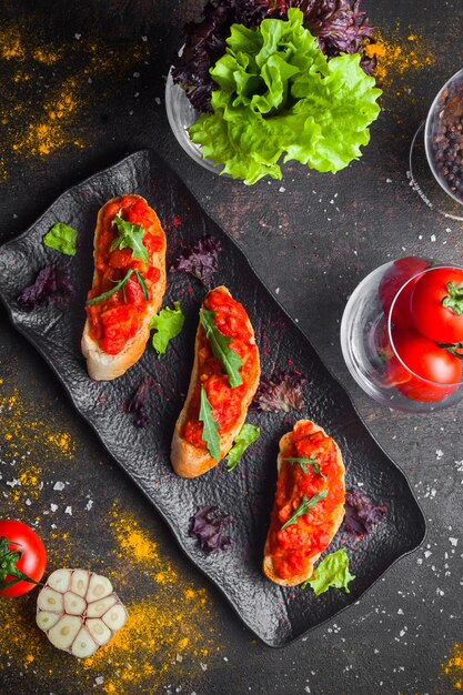 Collation vue de dessus avec salade de tomates et pain de mie et roquette en plaque sombre