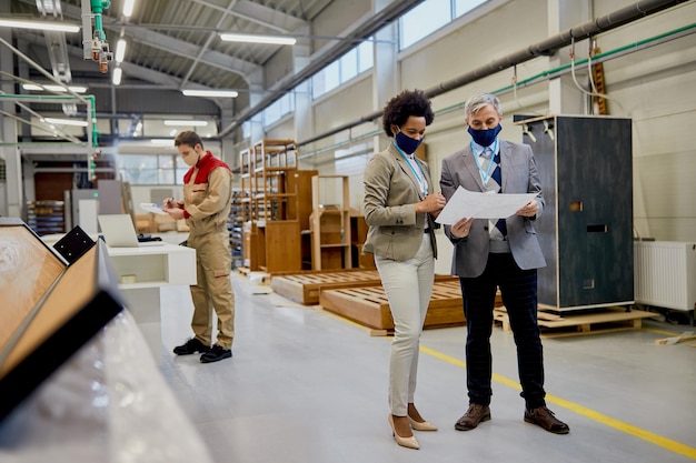 Collègues d'affaires analysant des plans lors de la visite d'une usine de bois pendant la pandémie de coronavirus