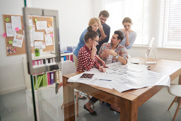 Collègues au bureau avec des plans d'architecture et un ordinateur