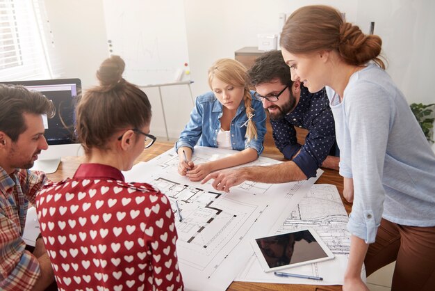 Collègues au bureau avec des plans d'architecture et un ordinateur