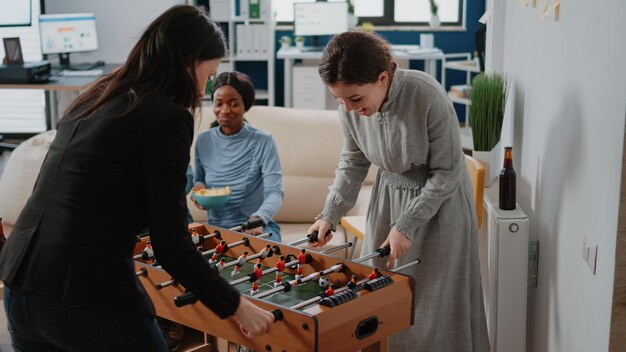 Collègues d'entreprise utilisant une table de baby-foot pour jouer au football, jouant après le travail au bureau. Collègues buvant des bouteilles de bière et d'alcool tout en profitant d'une activité pour s'amuser