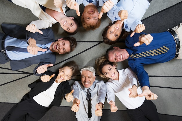 Collègues heureux couché sur le plancher, montrant thumbs up