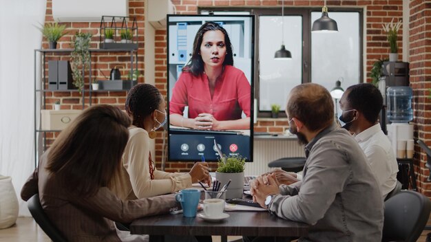 Collègues rencontrant une femme lors d'une conférence téléphonique vidéo, utilisant une téléconférence vidéo à distance sur moniteur. Les hommes d'affaires travaillant avec la vidéoconférence en ligne pendant la pandémie de covid 19.