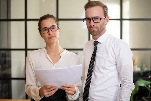 Des collègues sérieux tenant un document et regardant la caméra.