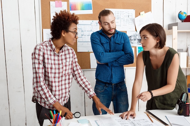 Photo gratuite des collègues souriant, parlant, discutant de dessins, de nouvelles idées au bureau