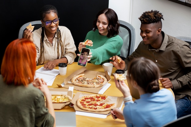 Photo gratuite collègues souriants à coup moyen mangeant de la pizza au travail